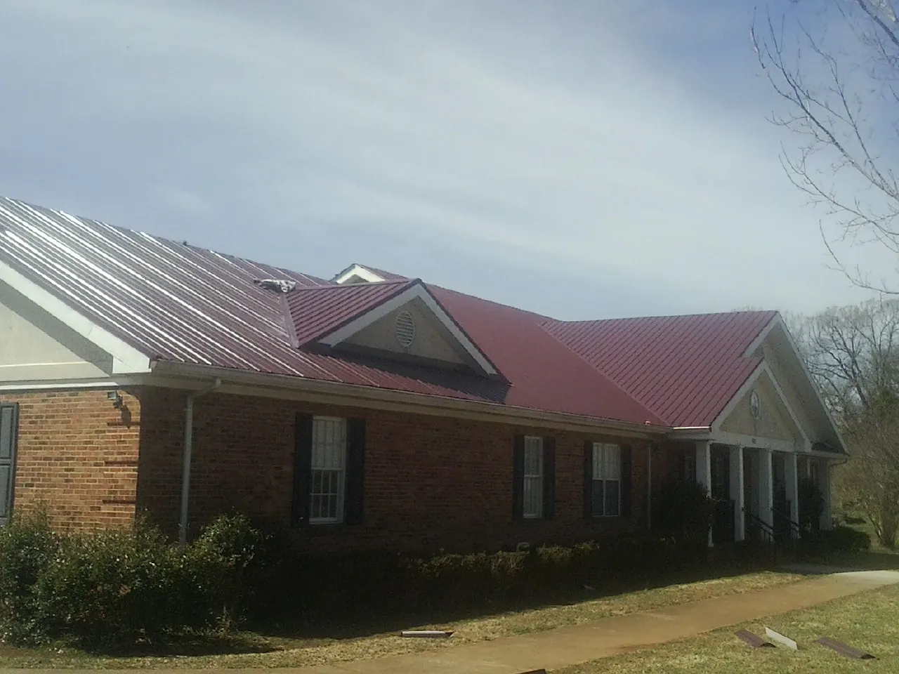 Red metal roof with gabled entries on a long brick building, from a Hail Damage Roof Repair job in Baton Rouge