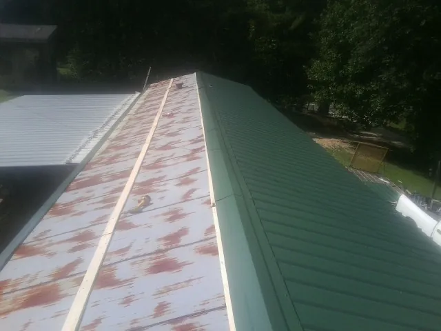 Old rusted panels beside newly installed green metal roofing — Wind Damage Roof Repair by Roofing Brothers in Baton Rouge