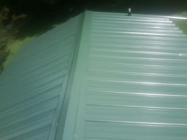 New green metal panels meeting at the ridge of a roof — Flat Roof Repair work by our crew in Baton Rouge