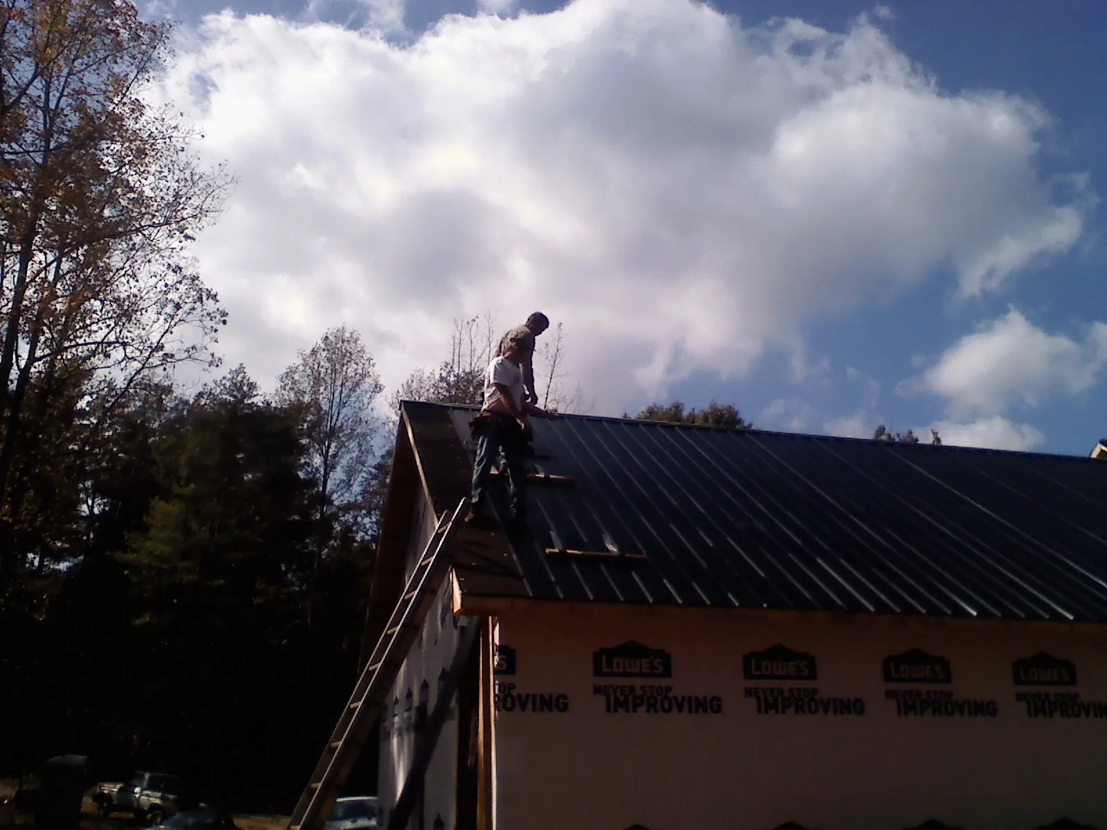 Roofer fastening dark metal panels high against a cloudy sky, from a Roof Inspection job in Baton Rouge
