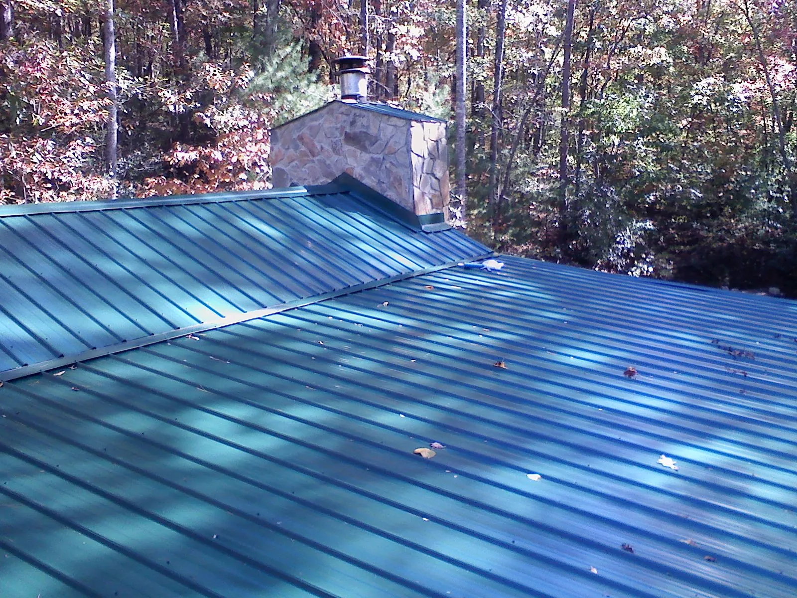 New green metal roof and stone chimney surrounded by autumn woods in Baton Rouge