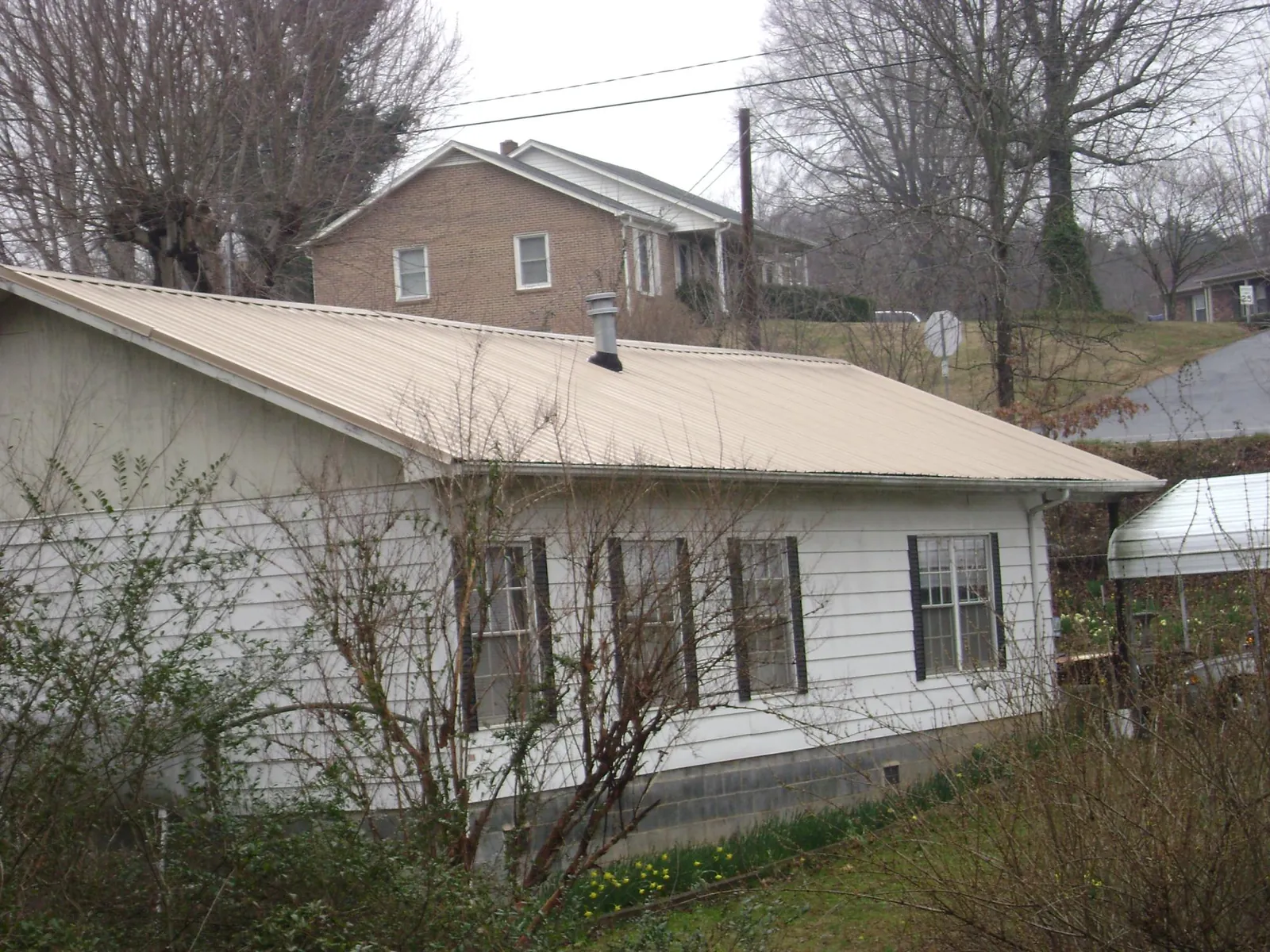 Tan metal roof on a white sided house set into a hillside — Commercial Roofing by Roofing Brothers in Baton Rouge
