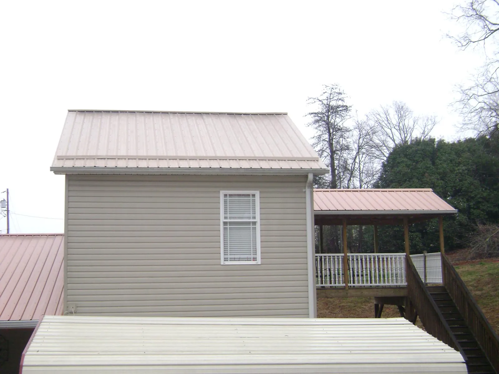 Tan metal roofs on a two story addition and attached porch, from a Roof Replacement job in Baton Rouge